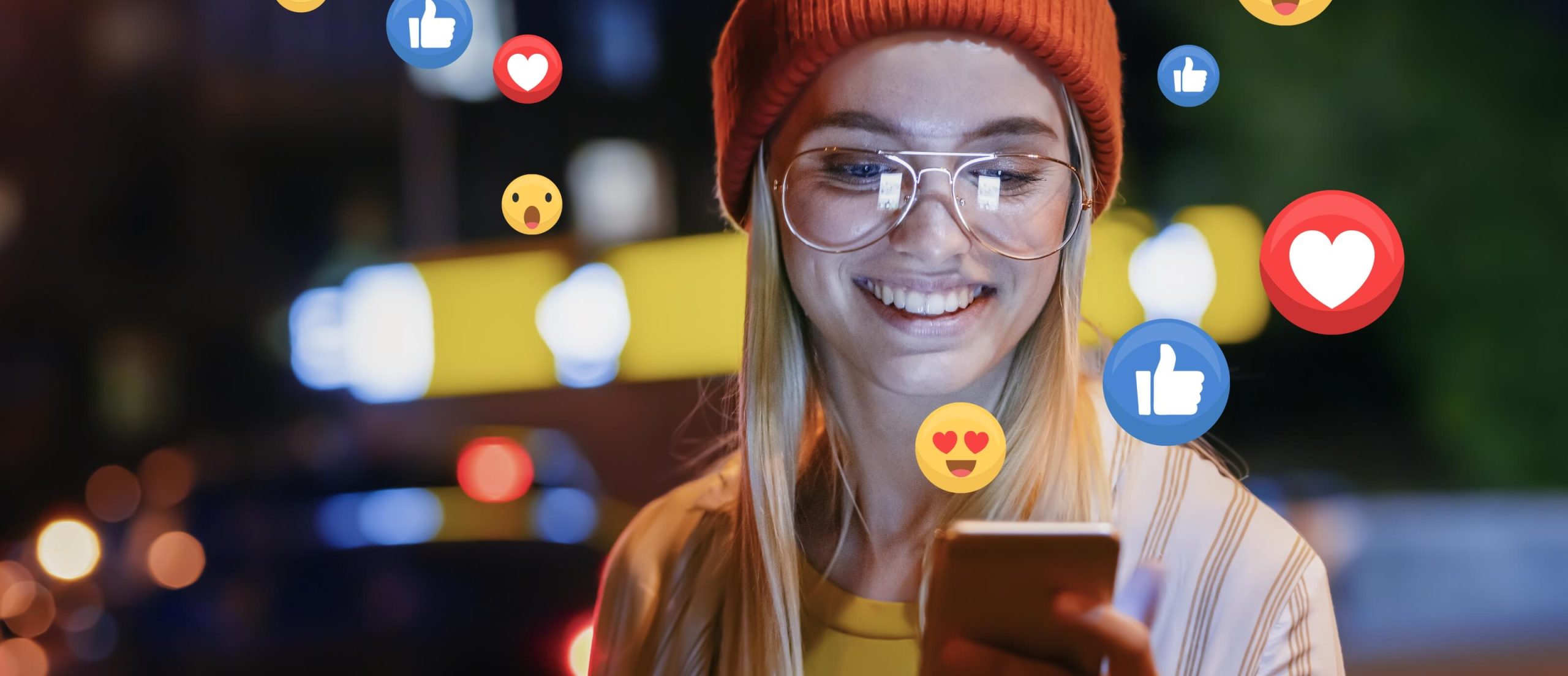Mädchen mit Brille lächelt auf ihr Handy und Emojis fliegen um sie herum